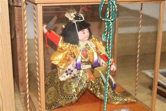 A Japanese wooden cased model of a Samurai warrior holding aloft a fan, with ornate silkwork robes, overall height 35cm, width 33cm